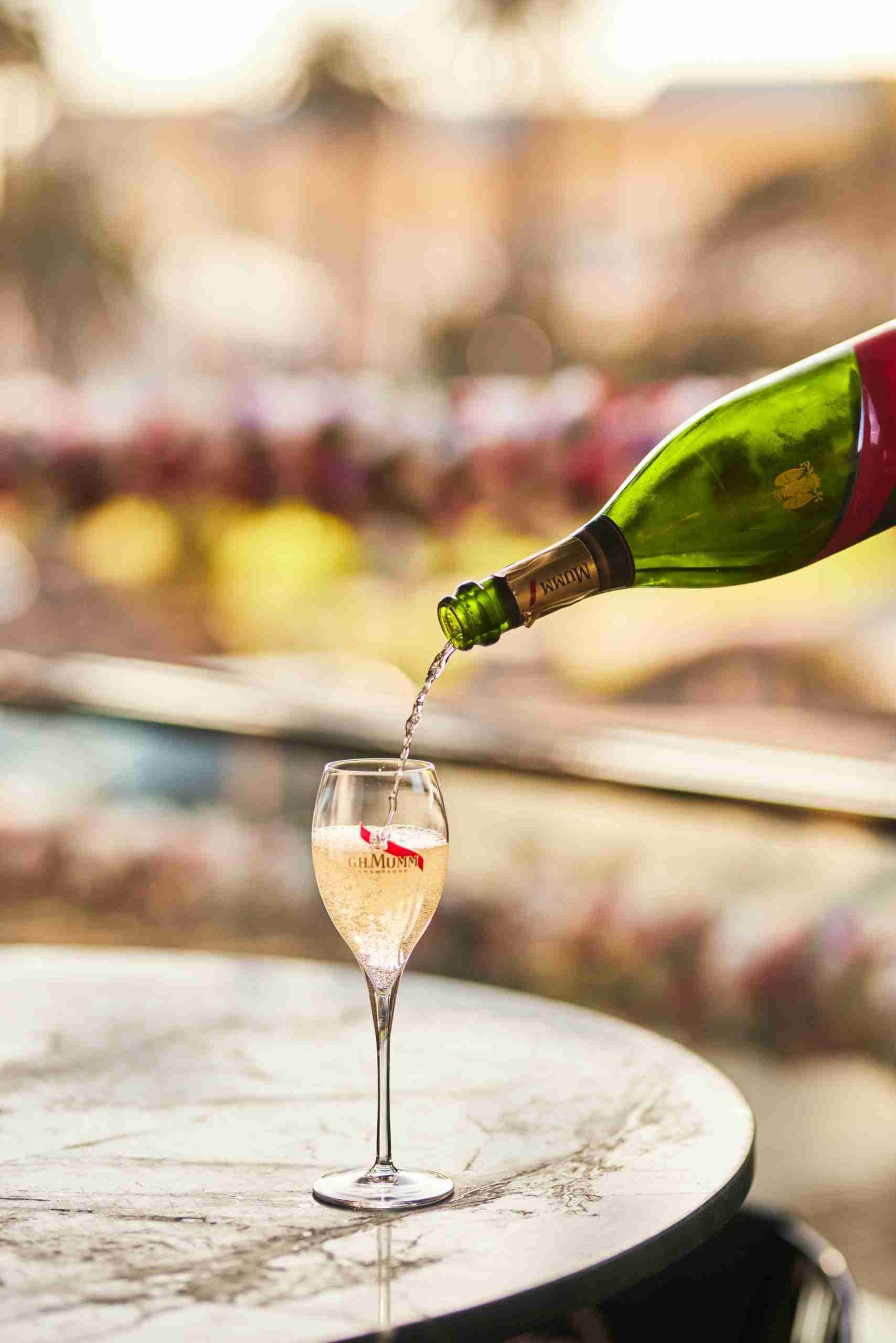 Bubbly flute of G.H. Mumm champagne being poured with vibrant bubbles, ready to toas with St Kilda background.