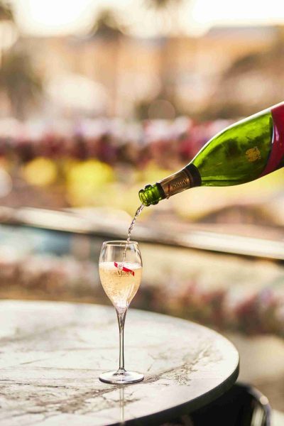 Bubbly flute of G.H. Mumm champagne being poured with vibrant bubbles, ready to toas with St Kilda background.